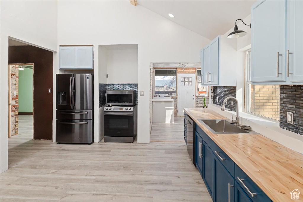 Kitchen with stainless steel appliances, blue cabinetry, high vaulted ceiling, wood counters, and tasteful backsplash