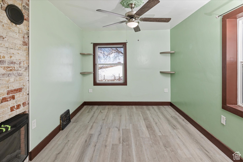 Empty room with wood finished floors, ceiling fan, and a glass covered fireplace