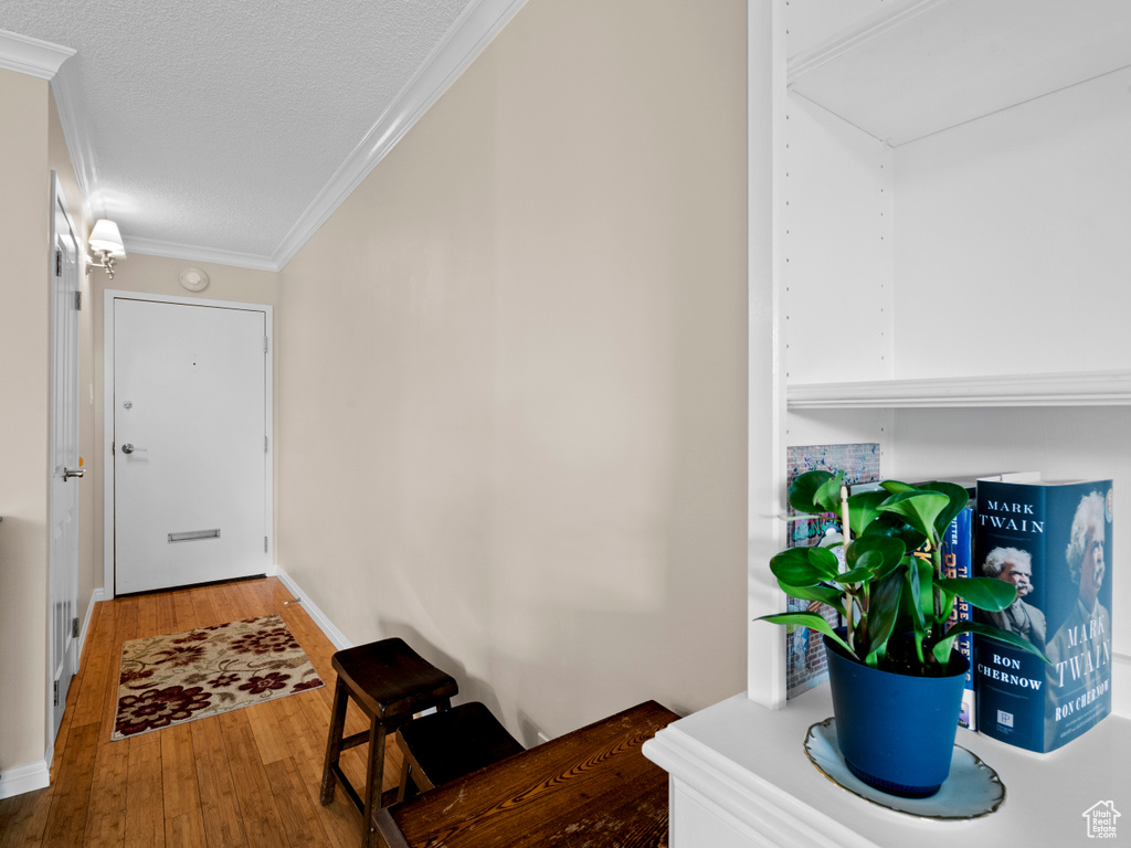 Hall featuring wood finished floors, a textured ceiling, crown molding, and attic access