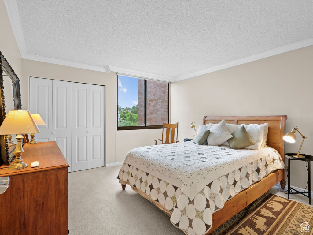 Bedroom with a textured ceiling, carpet floors, a closet, and crown molding