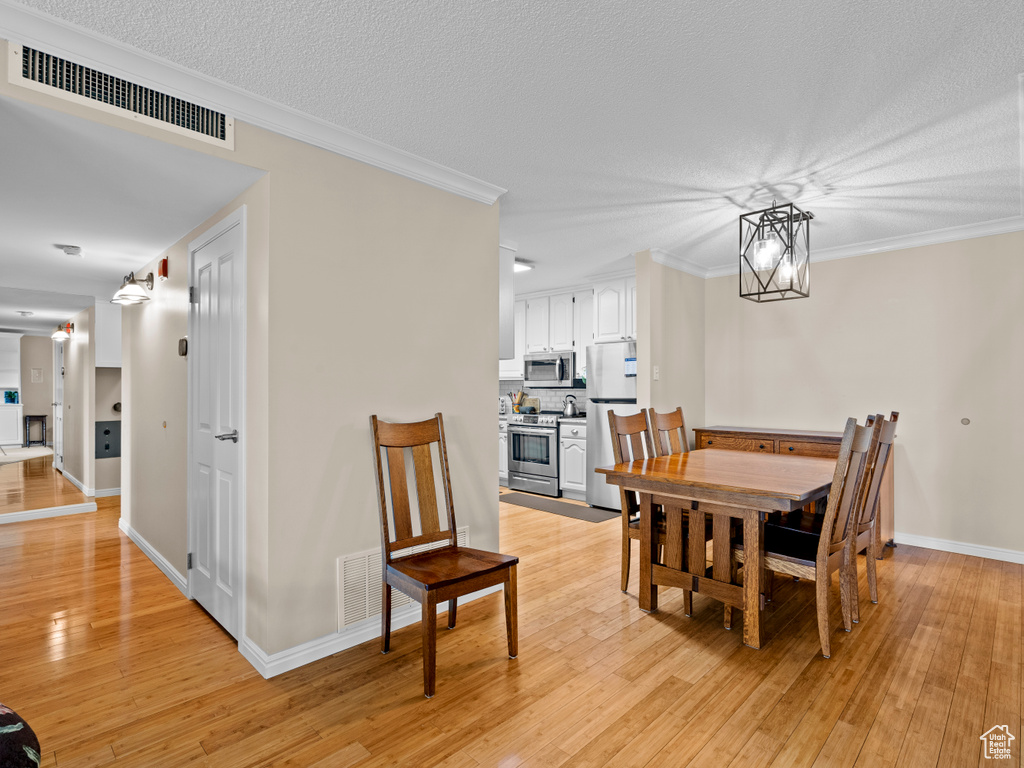 Dining area with light wood-style flooring, ornamental molding, a textured ceiling, and a chandelier