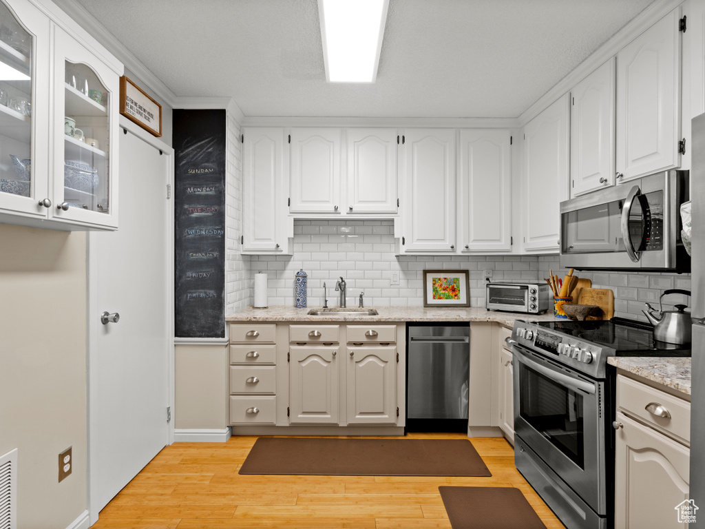 Kitchen featuring stainless steel appliances, decorative backsplash, white cabinets, and light wood-style floors