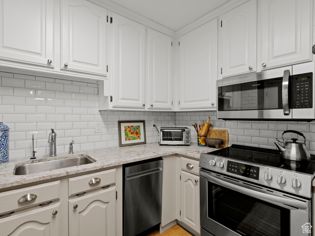 Kitchen with stainless steel appliances, white cabinets, light stone counters, and tasteful backsplash
