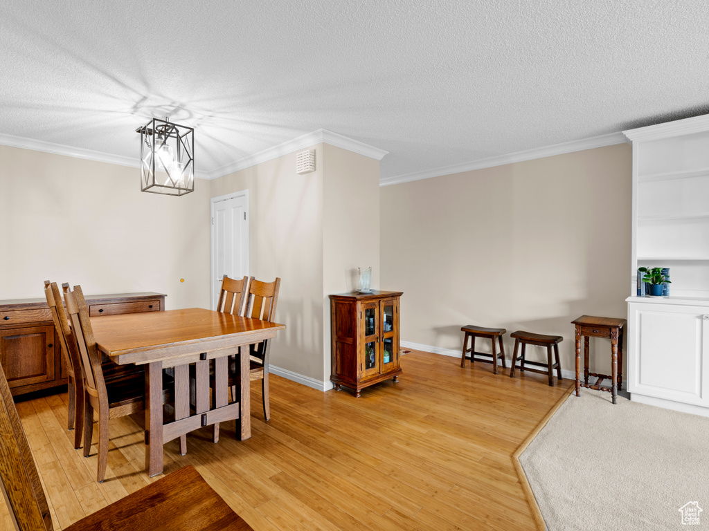Dining space featuring light wood-type flooring, a textured ceiling, and crown molding