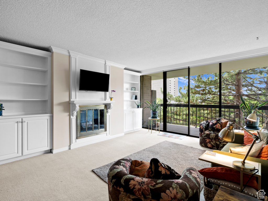 Living room featuring a textured ceiling, carpet, a glass covered fireplace, and built in features