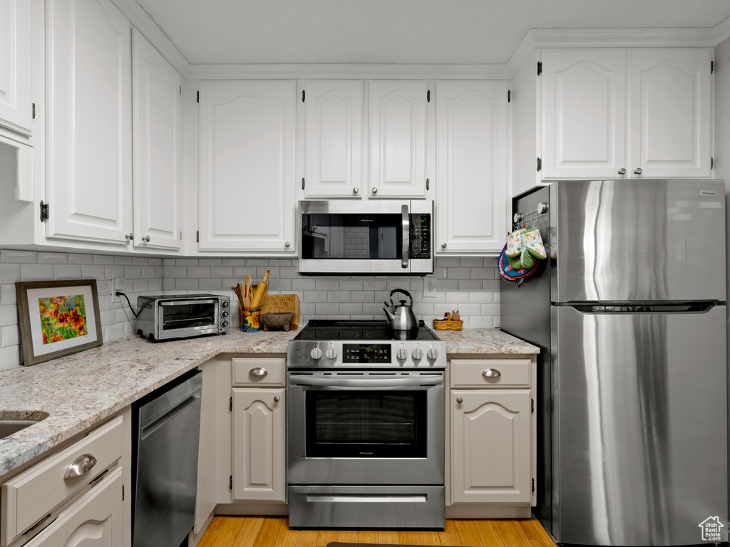 Kitchen with stainless steel appliances, decorative backsplash, and white cabinetry