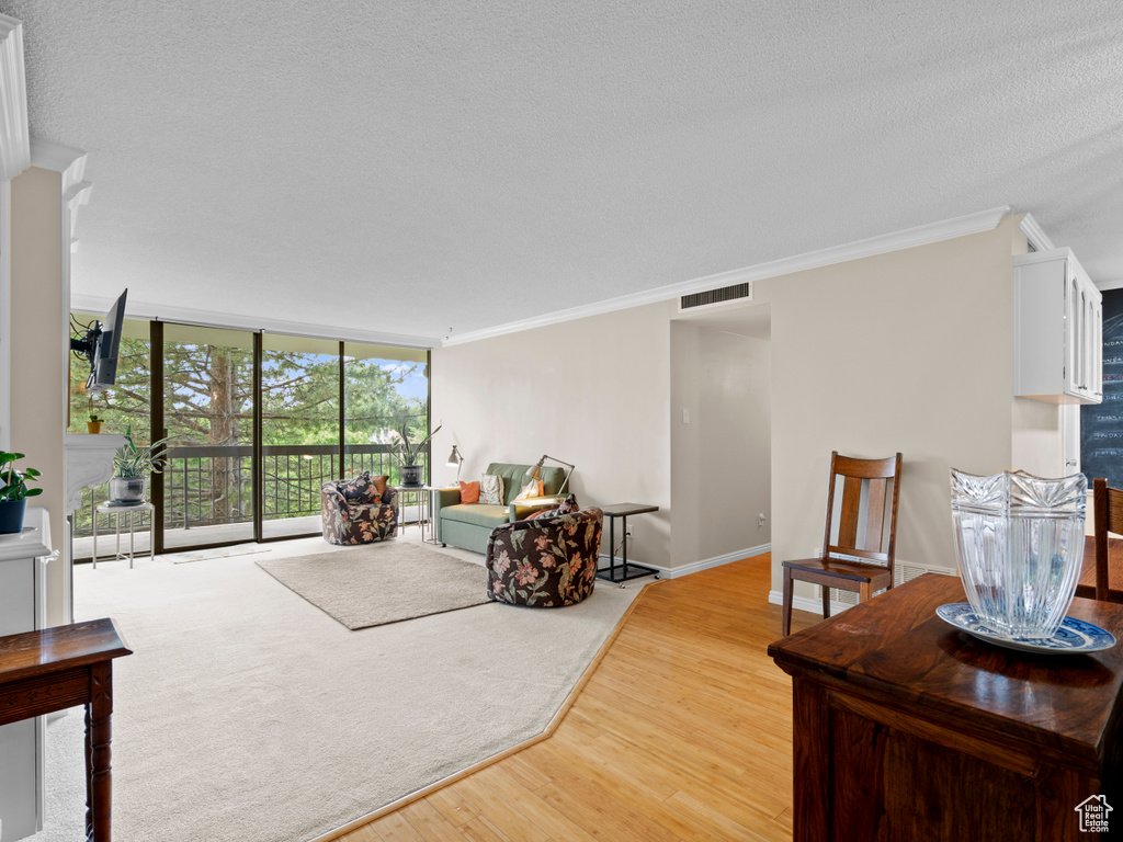 Living area featuring light wood finished floors, crown molding, a textured ceiling, and a wall of windows