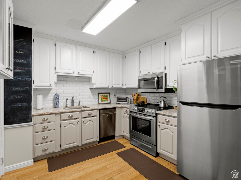 Kitchen featuring stainless steel appliances, light wood-type flooring, backsplash, and white cabinetry