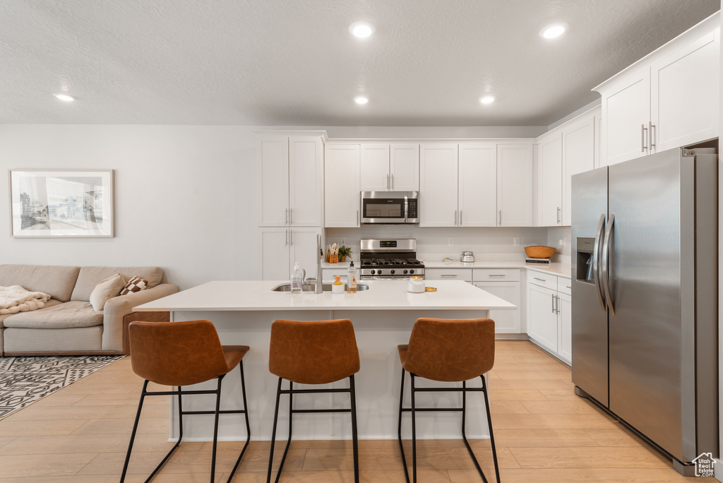 Kitchen with stainless steel appliances, light wood-style flooring, a breakfast bar, white cabinets, and recessed lighting