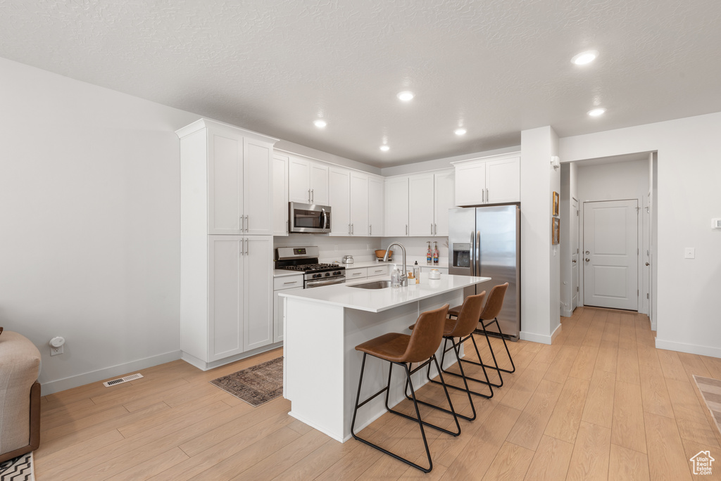 Kitchen with stainless steel appliances, light wood-type flooring, a breakfast bar, recessed lighting, and light countertops