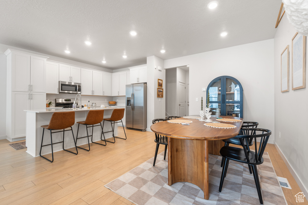Kitchen featuring stainless steel appliances, a center island with sink, a kitchen breakfast bar, light wood-style flooring, and white cabinetry
