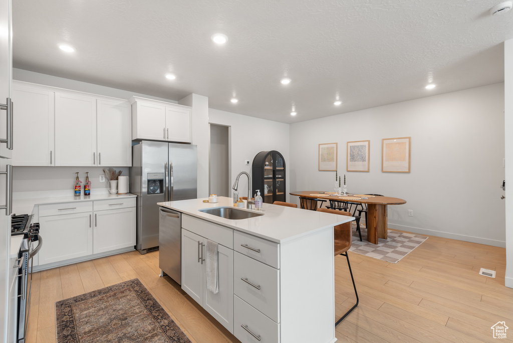 Kitchen featuring stainless steel appliances, light wood finished floors, recessed lighting, a center island with sink, and white cabinets