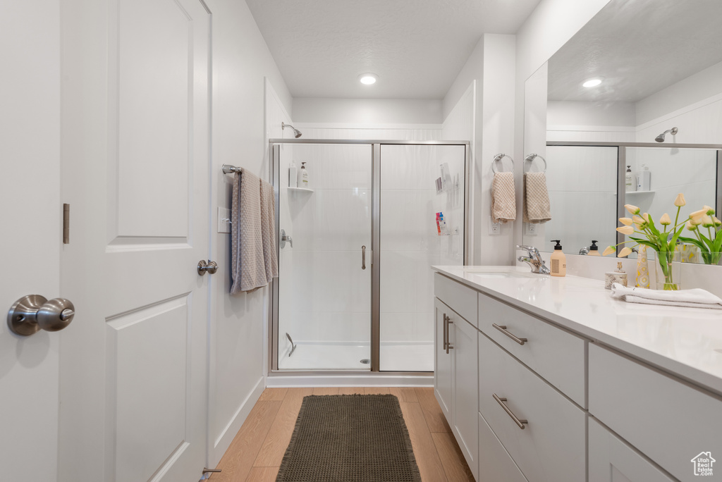 Full bath with a stall shower, wood finished floors, double vanity, and recessed lighting