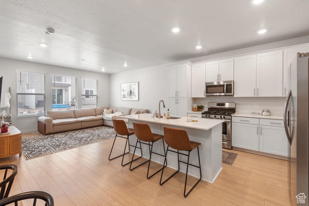 Kitchen with appliances with stainless steel finishes, a kitchen bar, open floor plan, light wood-style floors, and recessed lighting