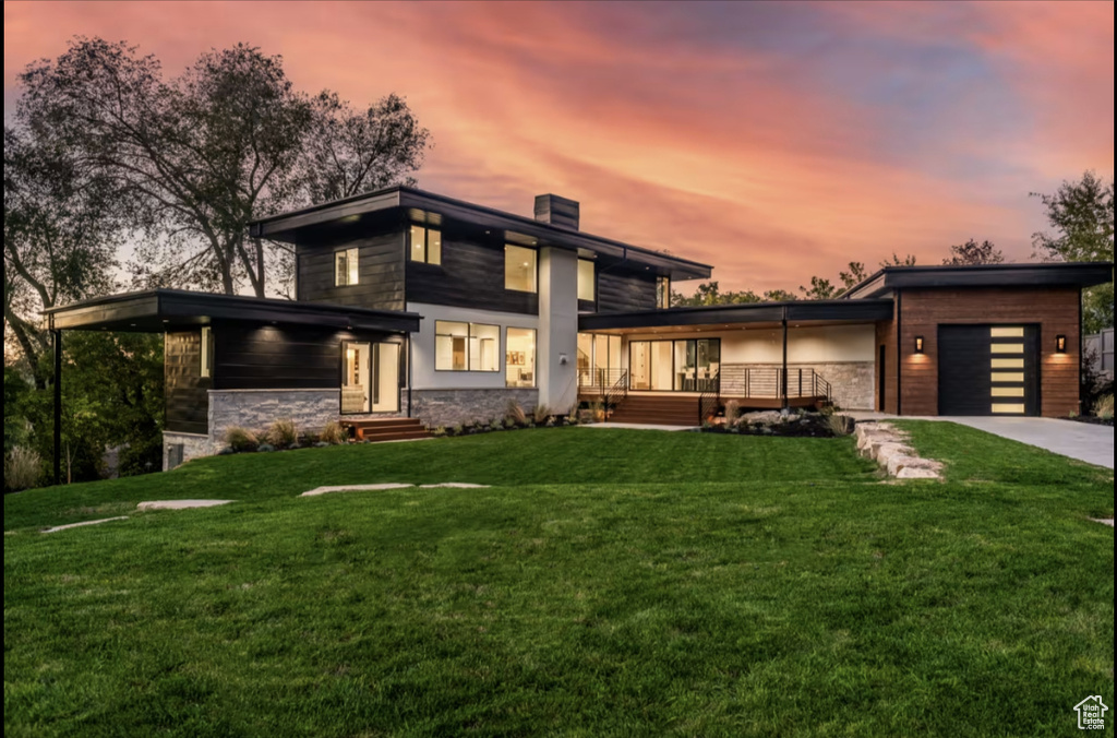 Contemporary home featuring an attached garage, driveway, a chimney, and a lawn