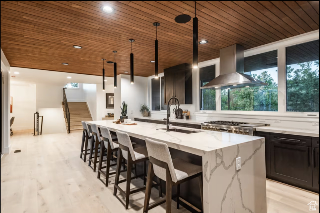 Kitchen featuring range hood, wood ceiling, healthy amount of natural light, a kitchen island with sink, and light stone countertops