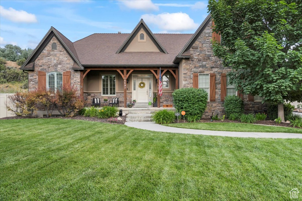 View of front of property featuring stone siding, a porch, a front lawn, and a shingled roof