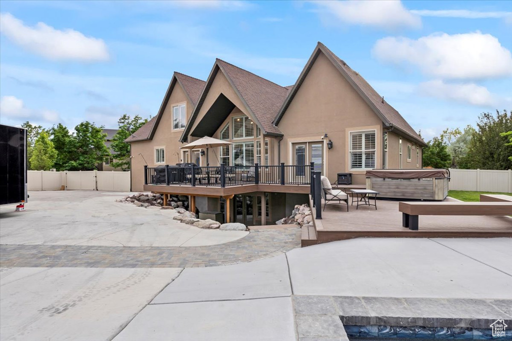 Rear view of property with a hot tub, stucco siding, a wooden deck, and a patio