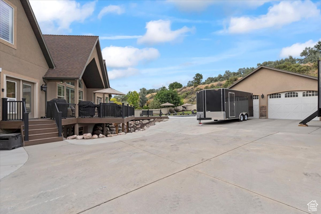 View of side of home featuring stucco siding, a deck, a garage, and a shingled roof