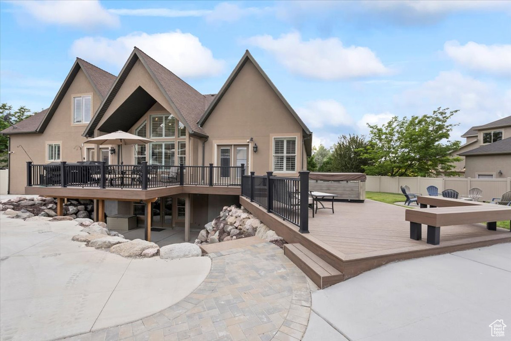 Back of house with a hot tub, a wooden deck, a patio area, and stucco siding