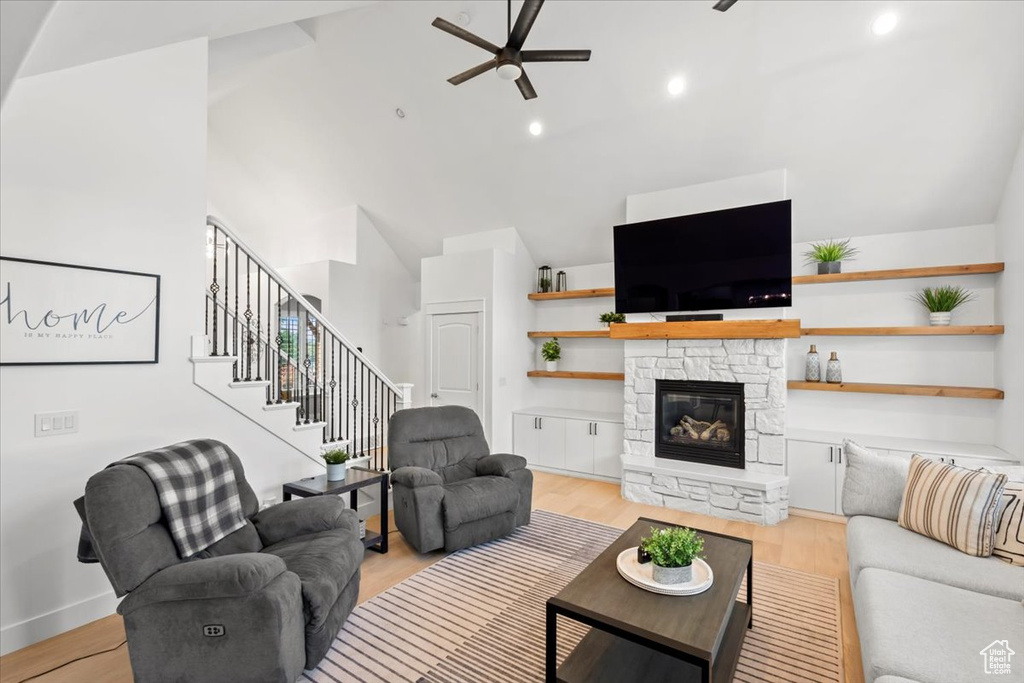 Living room featuring ceiling fan, a stone fireplace, stairway, light wood-style floors, and recessed lighting