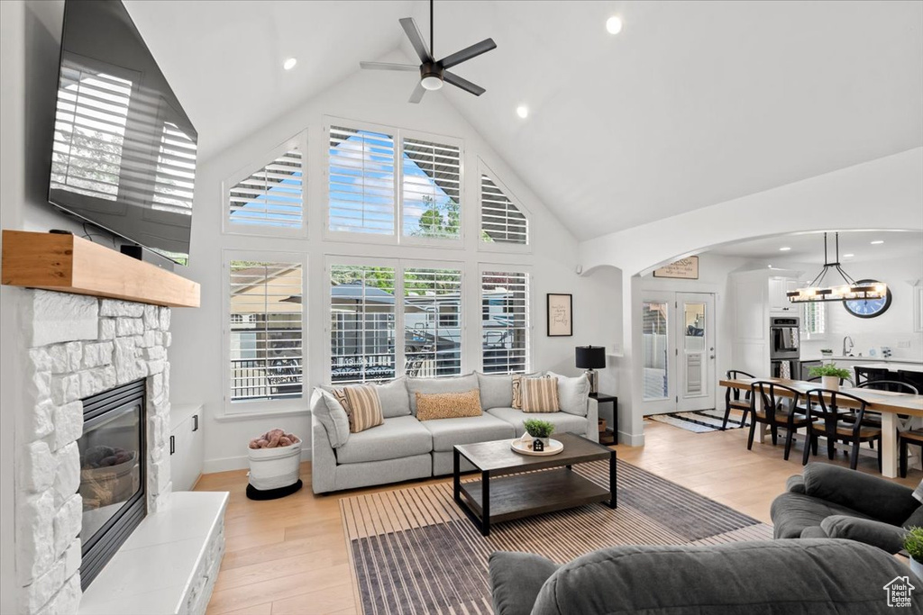 Living area with a stone fireplace, high vaulted ceiling, ceiling fan, light wood-type flooring, and a chandelier