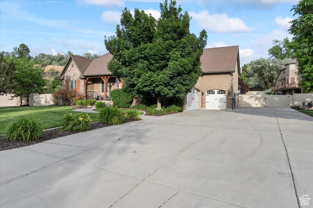 View of property hidden behind natural elements featuring driveway, a gate, and a garage