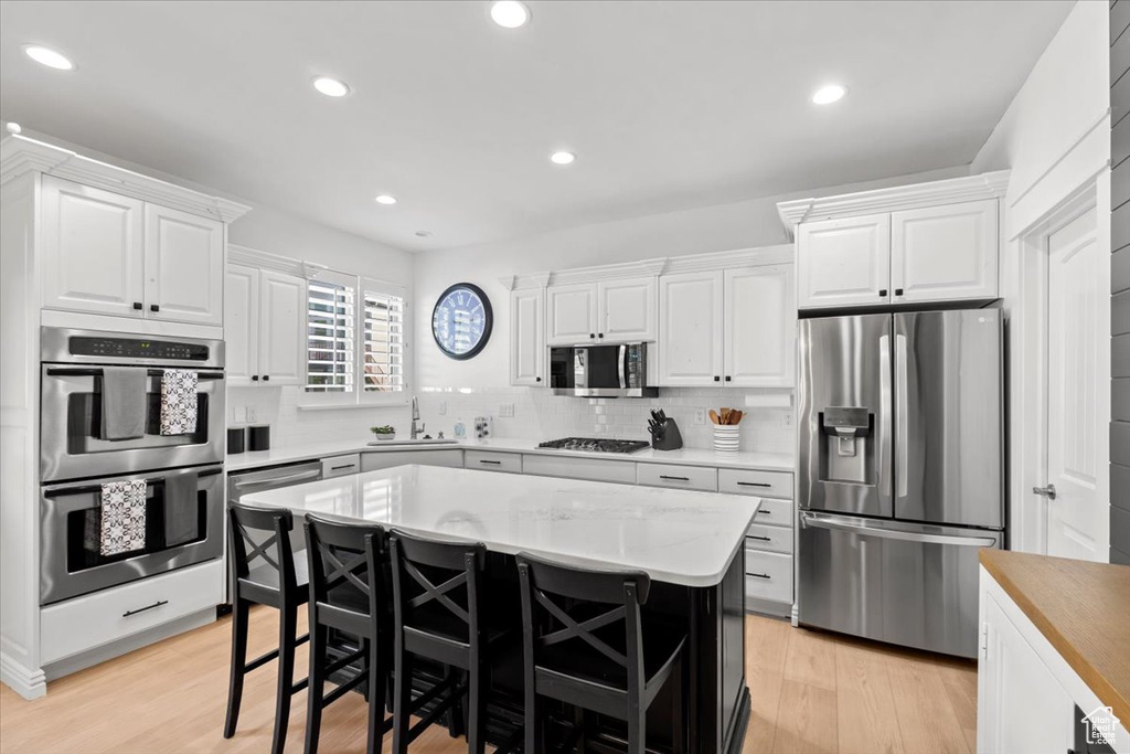 Kitchen with appliances with stainless steel finishes, white cabinets, light wood finished floors, light countertops, and recessed lighting