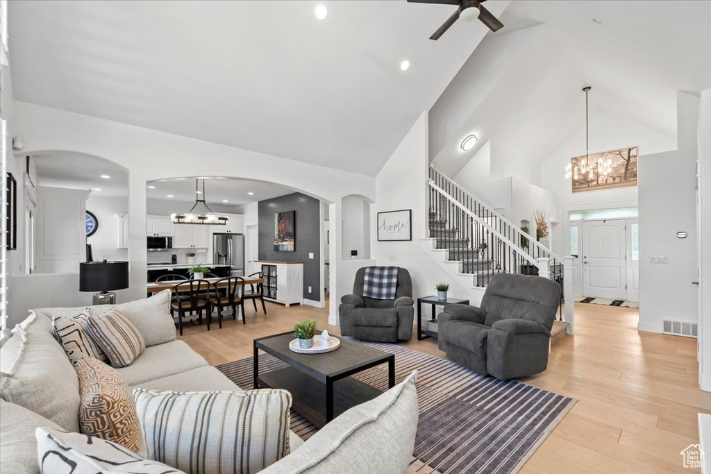 Living area with a chandelier, stairs, arched walkways, high vaulted ceiling, and ceiling fan