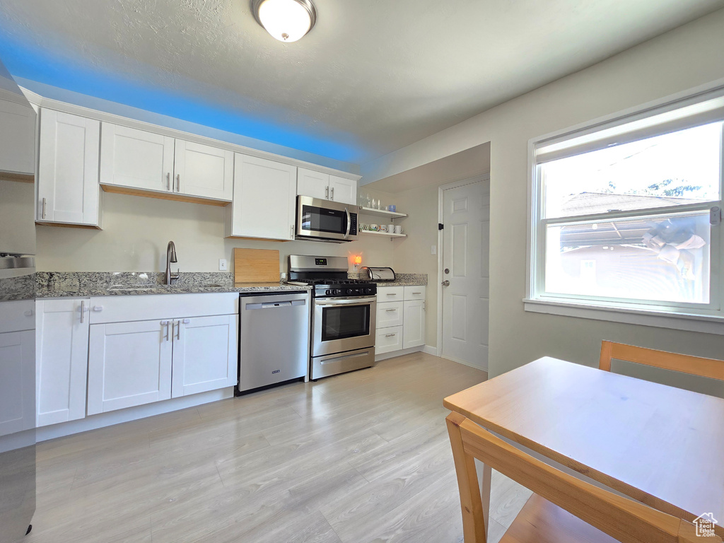 Kitchen with stainless steel appliances, light stone countertops, white cabinets, light wood-style floors, and open shelves