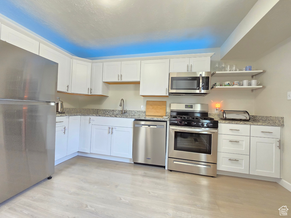 Kitchen with appliances with stainless steel finishes, light wood-type flooring, white cabinetry, and light stone counters