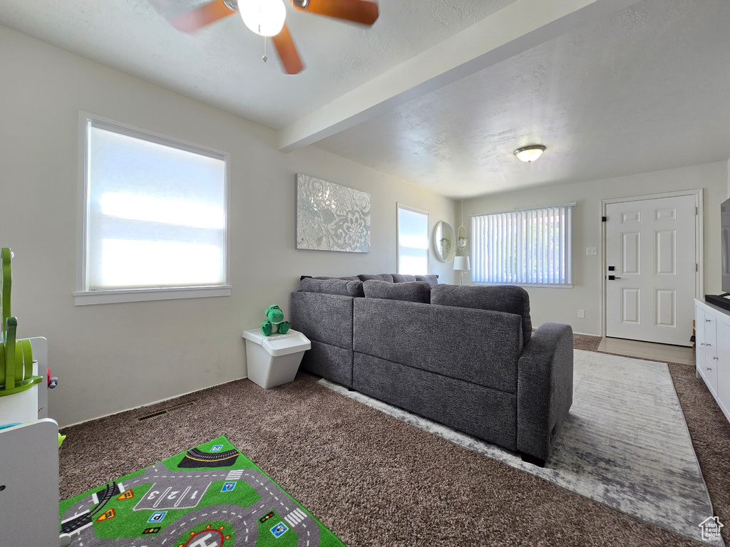Carpeted living room featuring plenty of natural light, ceiling fan, and beamed ceiling