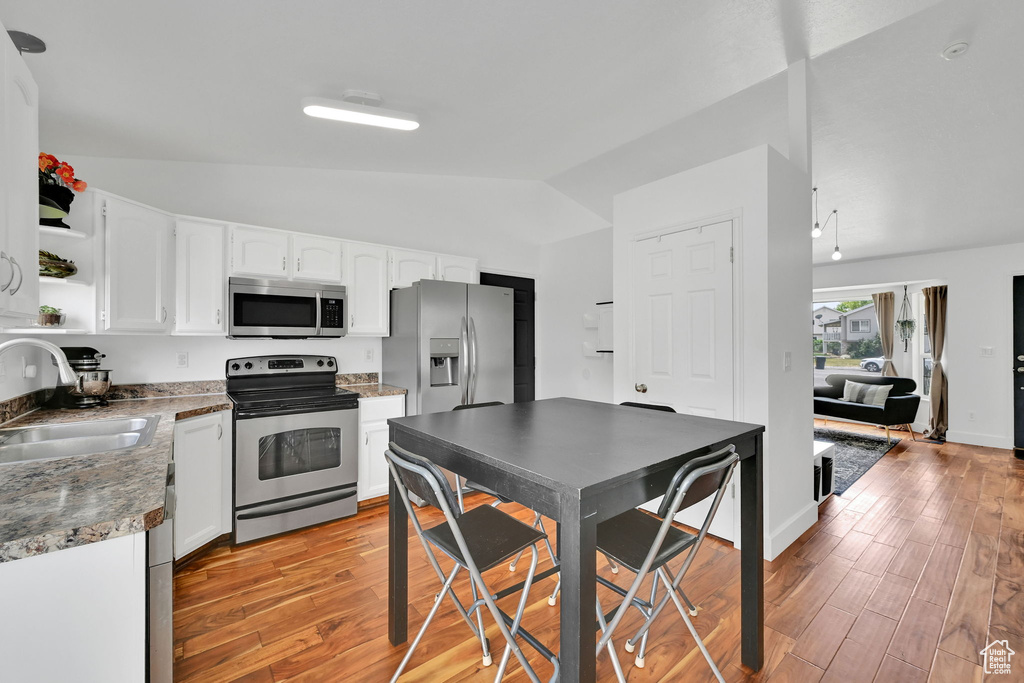 Kitchen with appliances with stainless steel finishes, vaulted ceiling, open shelves, light wood-type flooring, and white cabinets