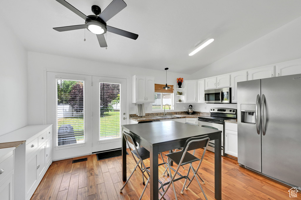 Kitchen featuring stainless steel appliances, white cabinetry, vaulted ceiling, light wood finished floors, and plenty of natural light