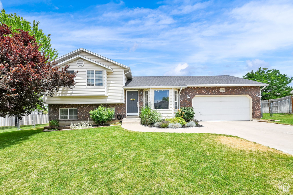 Tri-level home featuring brick siding, a garage, driveway, and roof with shingles