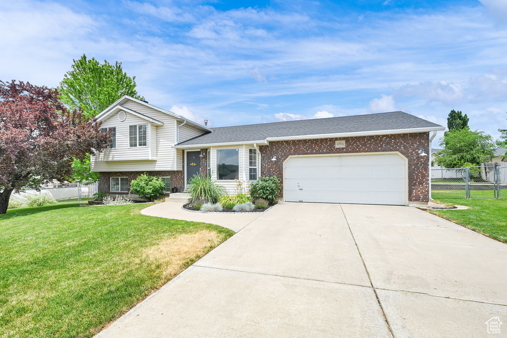 Split level home featuring brick siding, an attached garage, concrete driveway, and a shingled roof