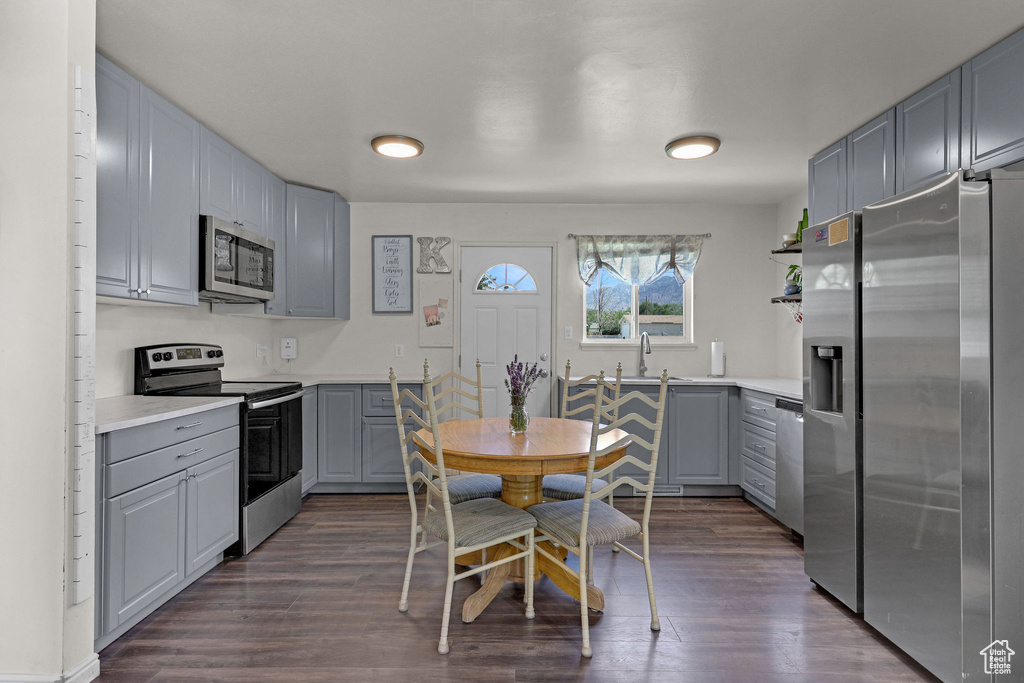 Kitchen with appliances with stainless steel finishes, gray cabinets, dark wood-style floors, light countertops, and open shelves