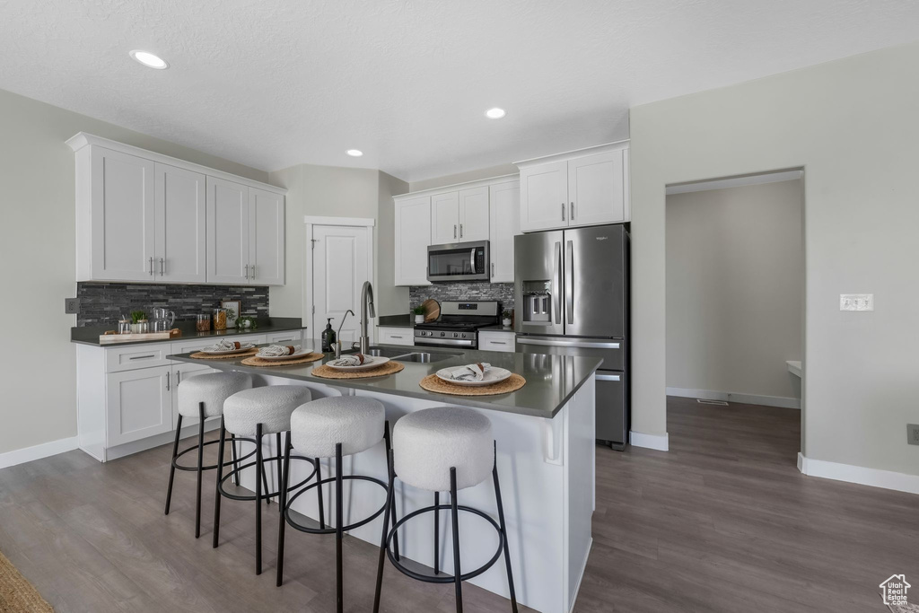 Kitchen with stainless steel appliances, dark countertops, tasteful backsplash, white cabinetry, and recessed lighting