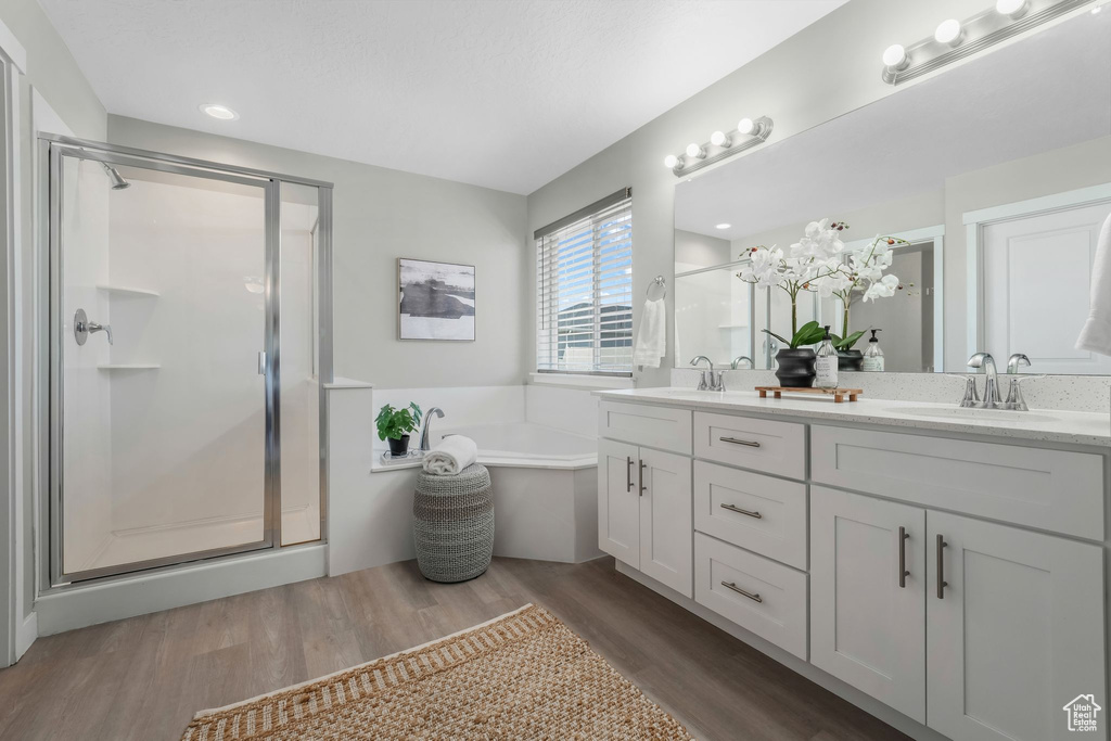 Bathroom with a shower stall, double vanity, a bath, and wood finished floors