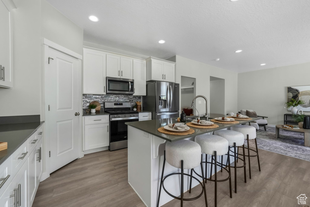 Kitchen featuring stainless steel appliances, dark countertops, a breakfast bar, dark wood-style flooring, and recessed lighting