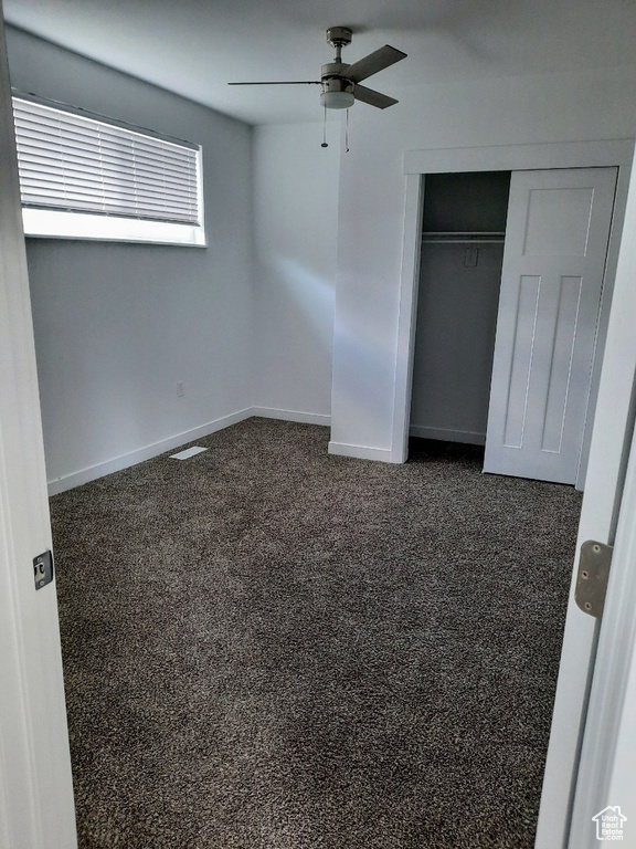 Unfurnished bedroom with a closet, a ceiling fan, and dark colored carpet