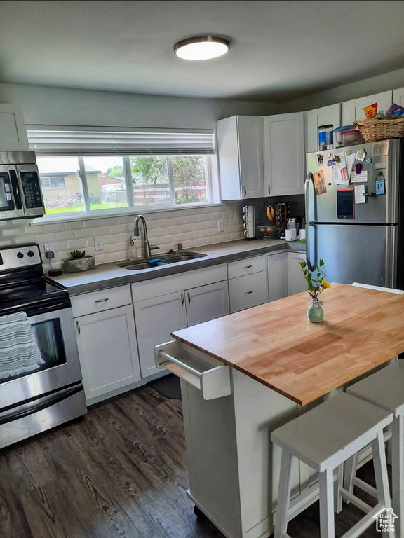 Kitchen featuring stainless steel appliances, white cabinetry, decorative backsplash, dark wood-style flooring, and wood counters