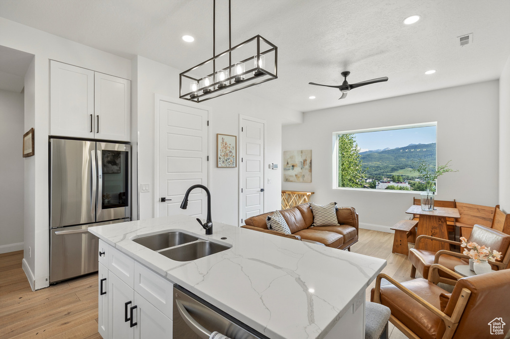 Kitchen with appliances with stainless steel finishes, open floor plan, white cabinets, light wood-type flooring, and recessed lighting