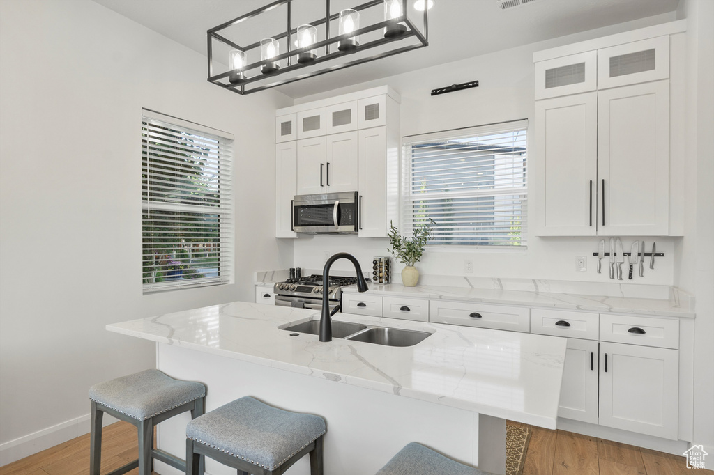 Kitchen with stainless steel appliances, light wood-style flooring, a kitchen breakfast bar, and white cabinets