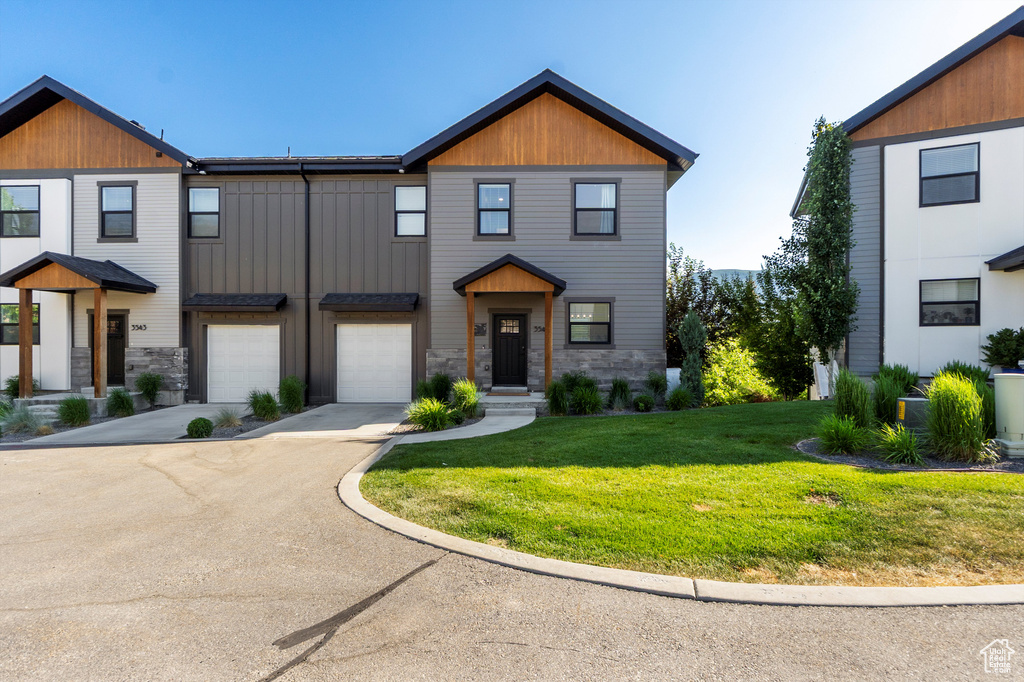 View of front of house with driveway, an attached garage, a front yard, and stone siding
