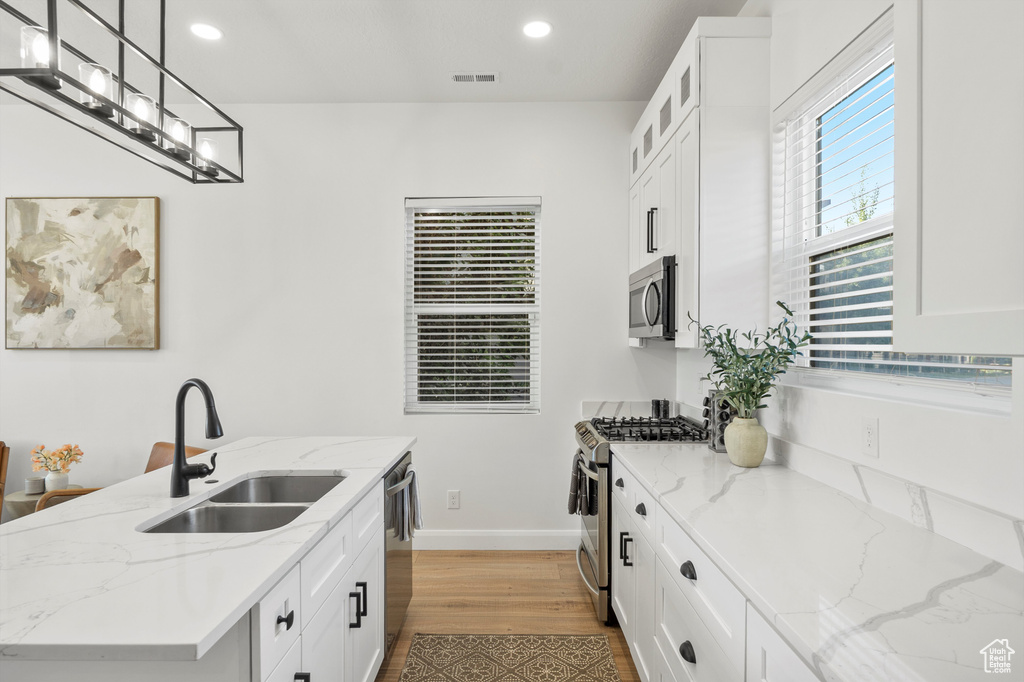 Kitchen featuring stainless steel appliances, wood finished floors, recessed lighting, white cabinets, and hanging light fixtures