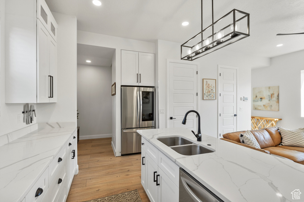 Kitchen with stainless steel appliances, light wood finished floors, white cabinetry, glass insert cabinets, and recessed lighting