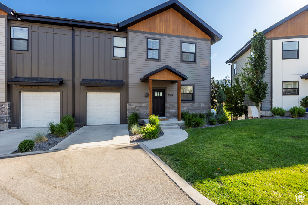 View of property featuring driveway, a front lawn, an attached garage, and board and batten siding