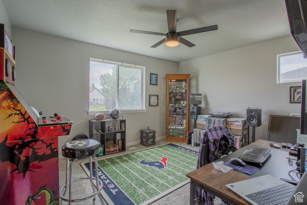 Carpeted home office featuring a ceiling fan and plenty of natural light