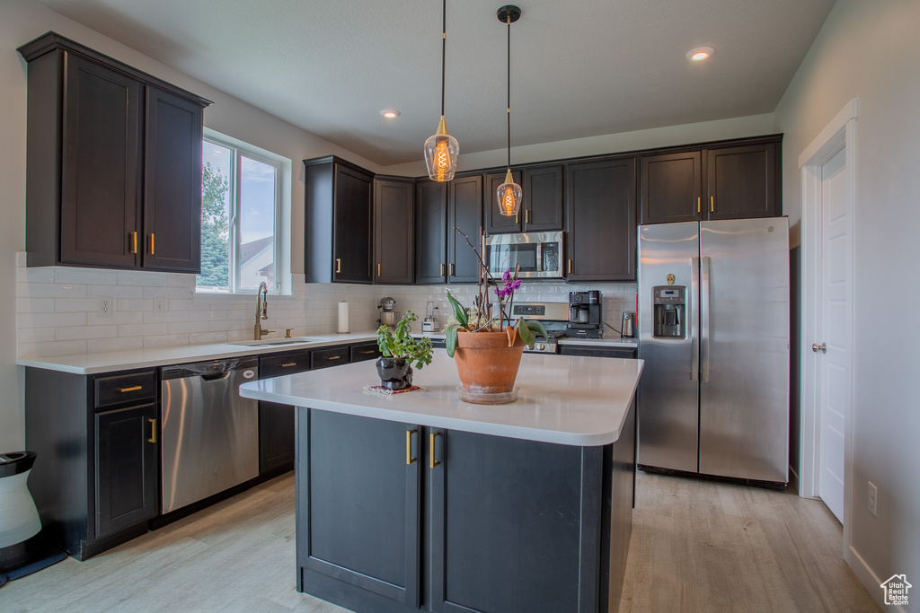 Kitchen with stainless steel appliances, light wood-style flooring, light countertops, backsplash, and a kitchen island